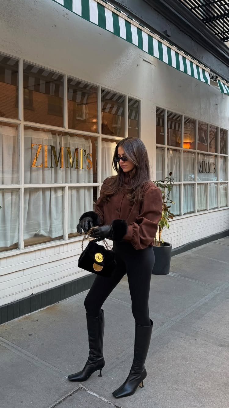 Woman in a brown top and black leggings posing on a city sidewalk near a storefront.