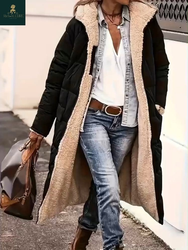 A person wearing a long black puffer coat with faux fur lining and blue jeans.