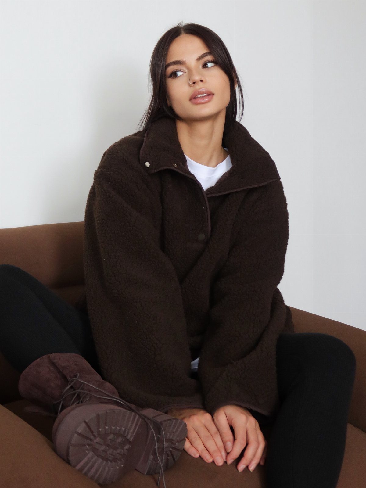 A woman wearing a brown fleece jacket and black leggings sitting on a brown sofa.