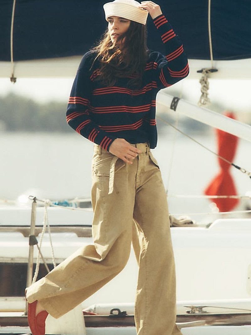 A woman in a navy and red striped sweater and tan trousers posing on a sailboat.