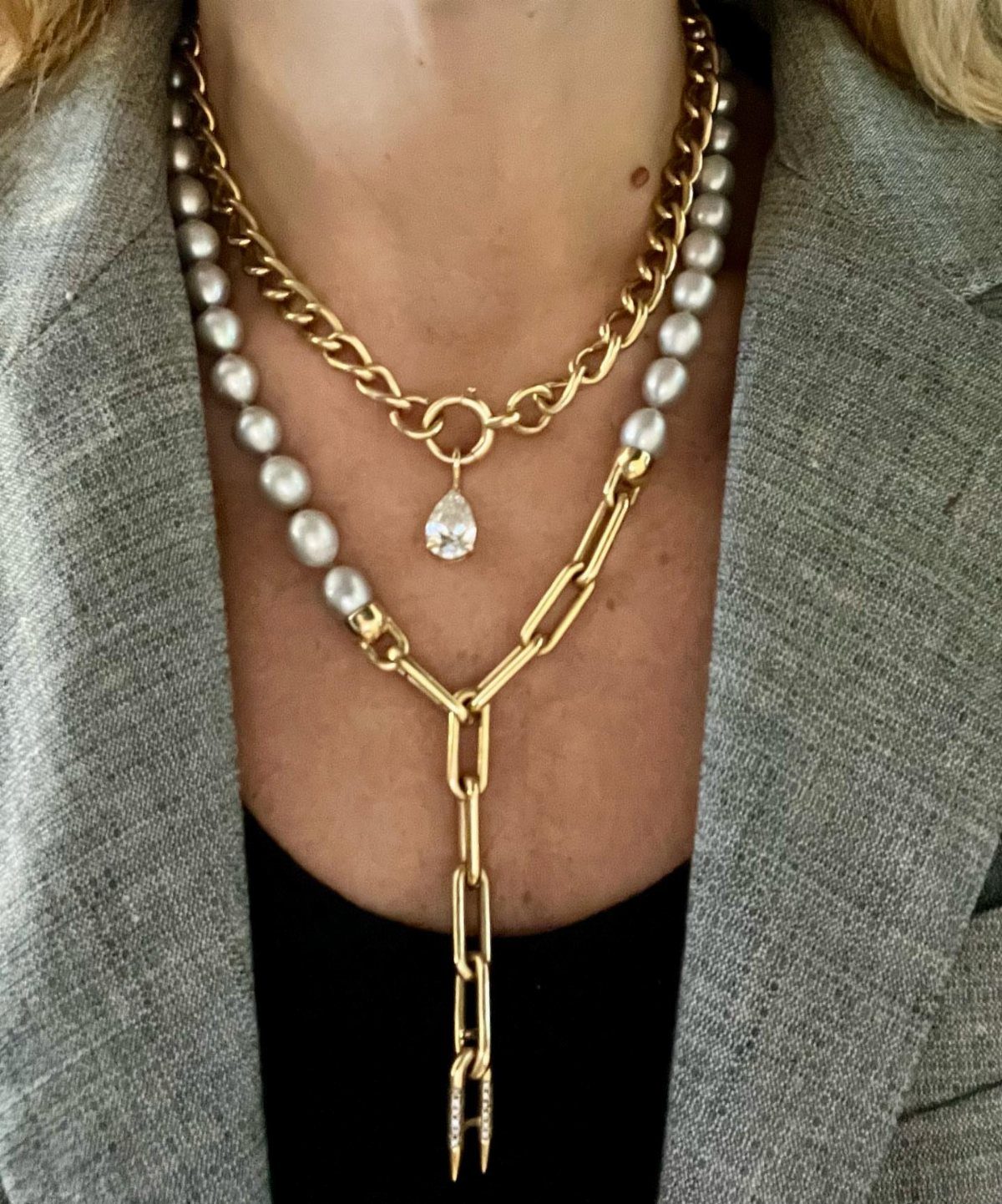 Layered gold and pearl necklaces worn over a grey blazer and black top.