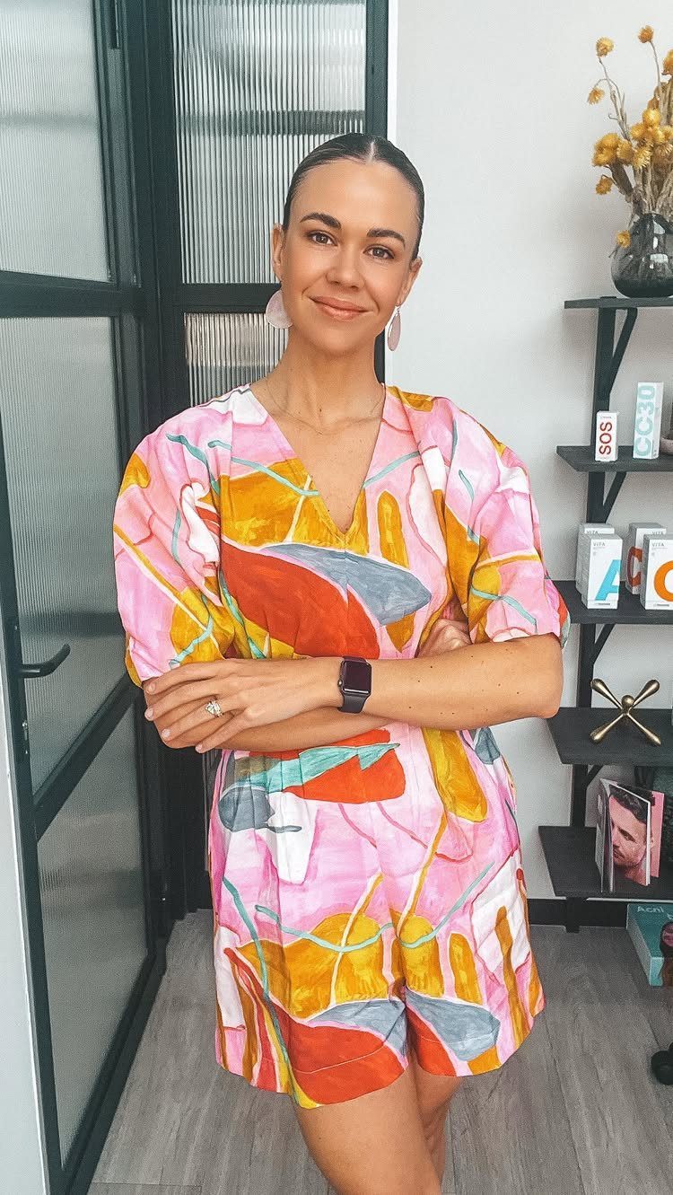 A smiling woman wearing a colorful abstract print short romper standing indoors.