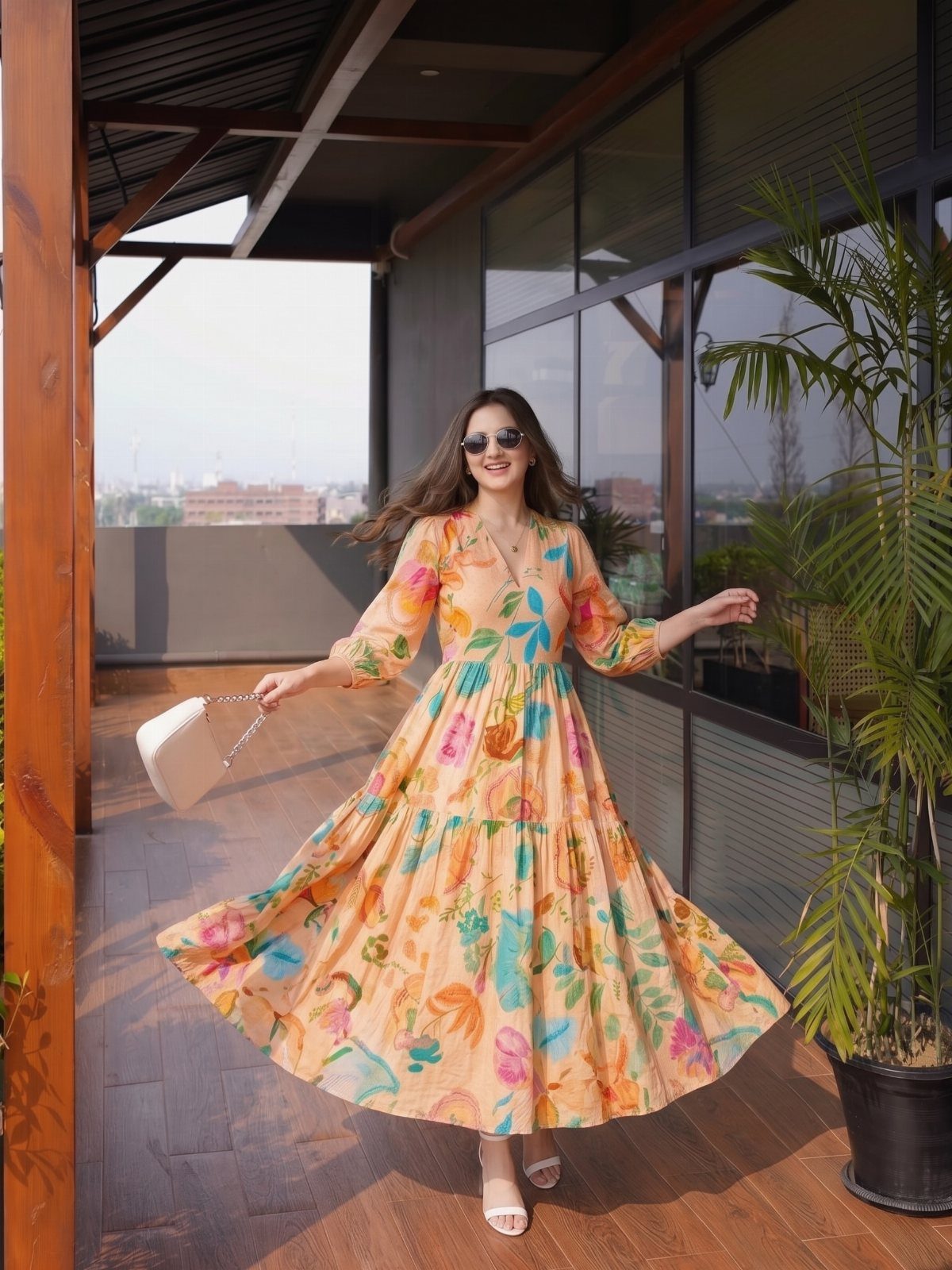 A woman in a peach floral printed midi dress and white sandals twirling on a balcony.