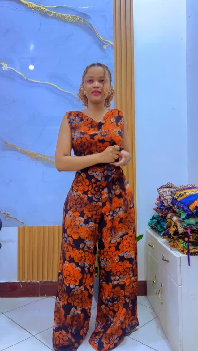 A woman posing in a sleeveless orange and black floral print wide-leg jumpsuit.