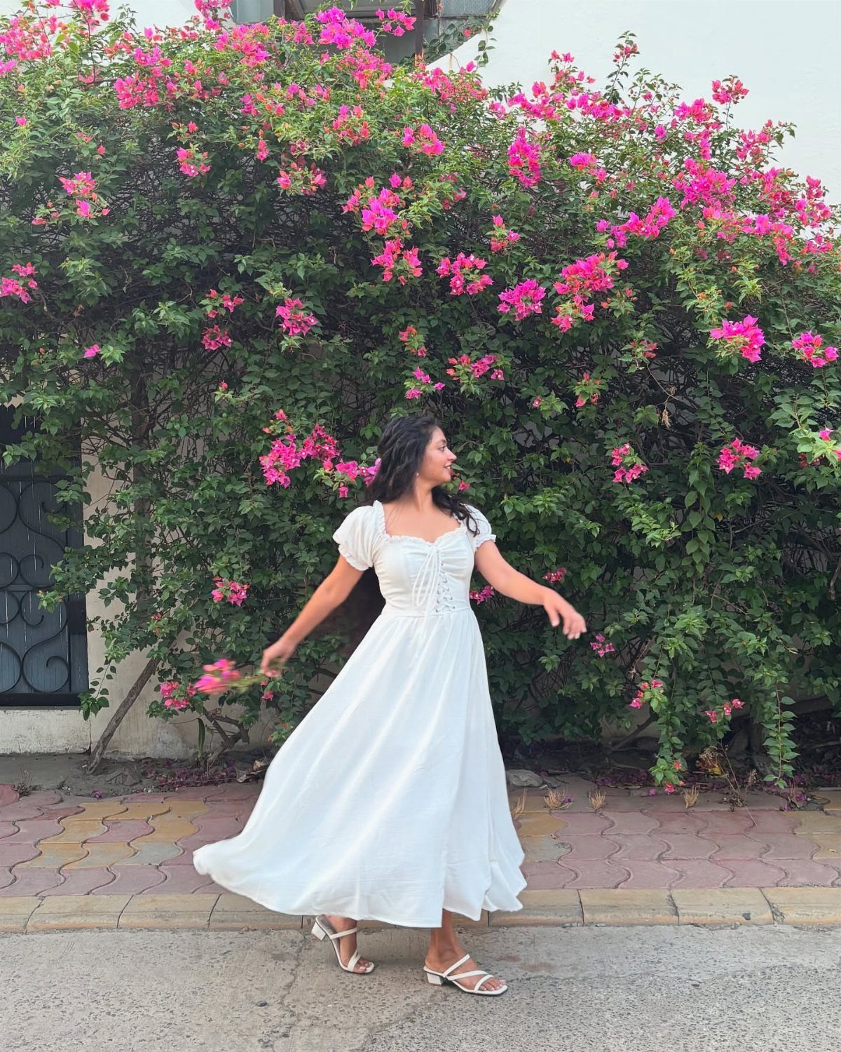 A woman wearing a white textured midi dress posing in front of pink flowers.