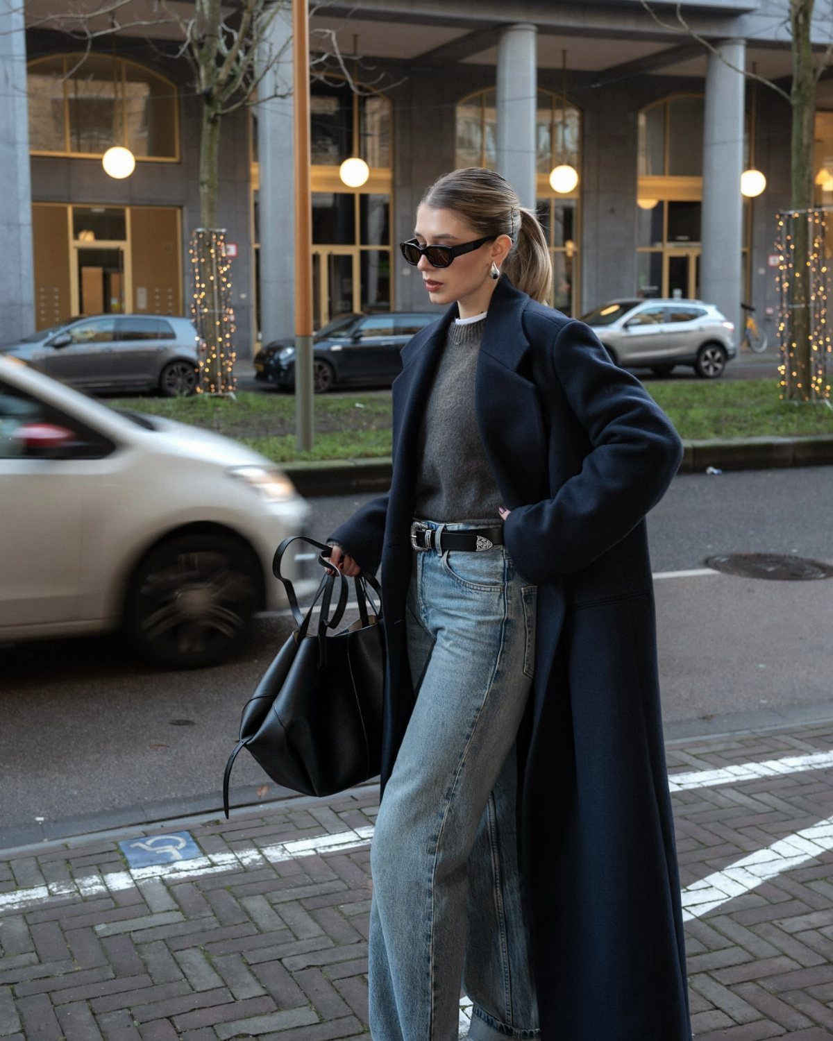 Woman walking in a city wearing a long navy wool coat over a grey sweater and jeans.