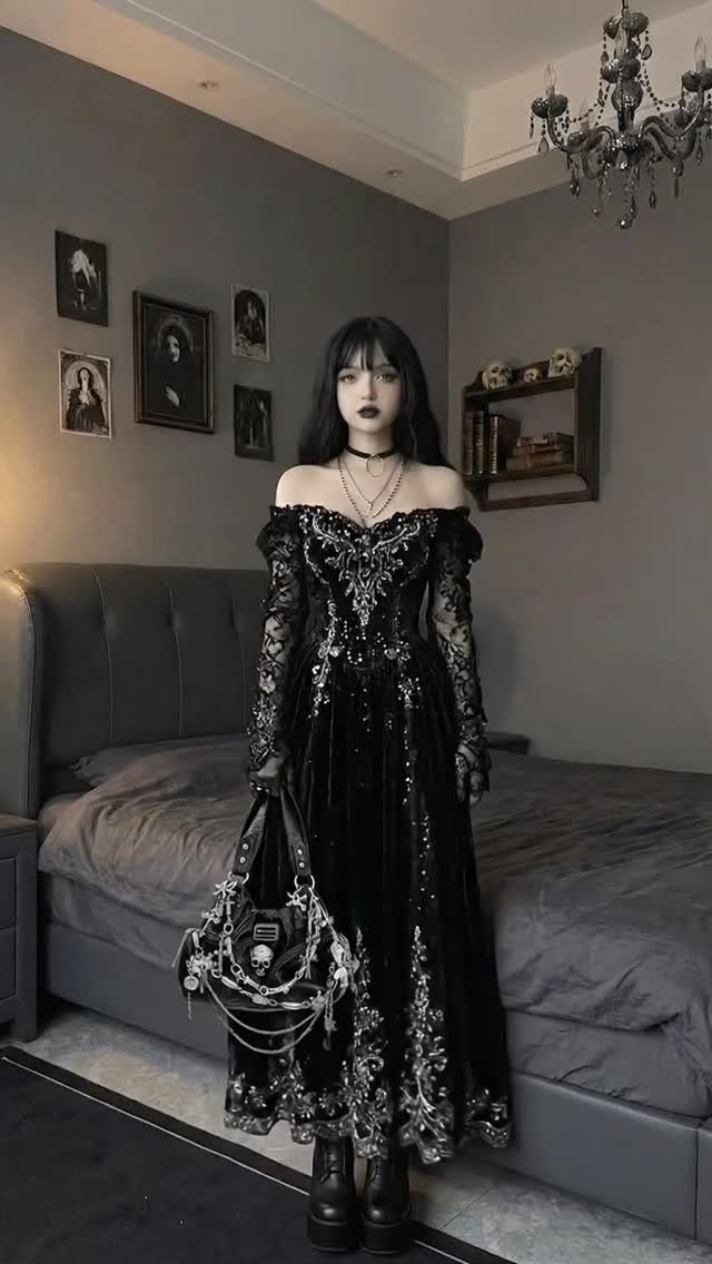 Woman in an ornate black velvet gown with silver embroidery standing in a grey bedroom.