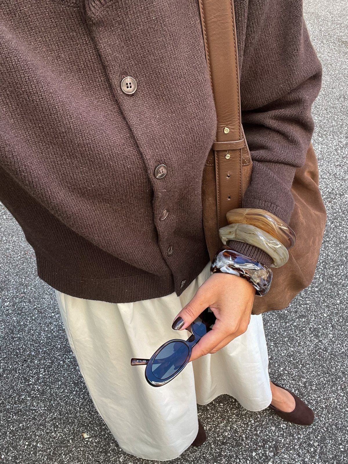 Person wearing a brown cardigan, white skirt, brown loafers, and carrying a leather bag.