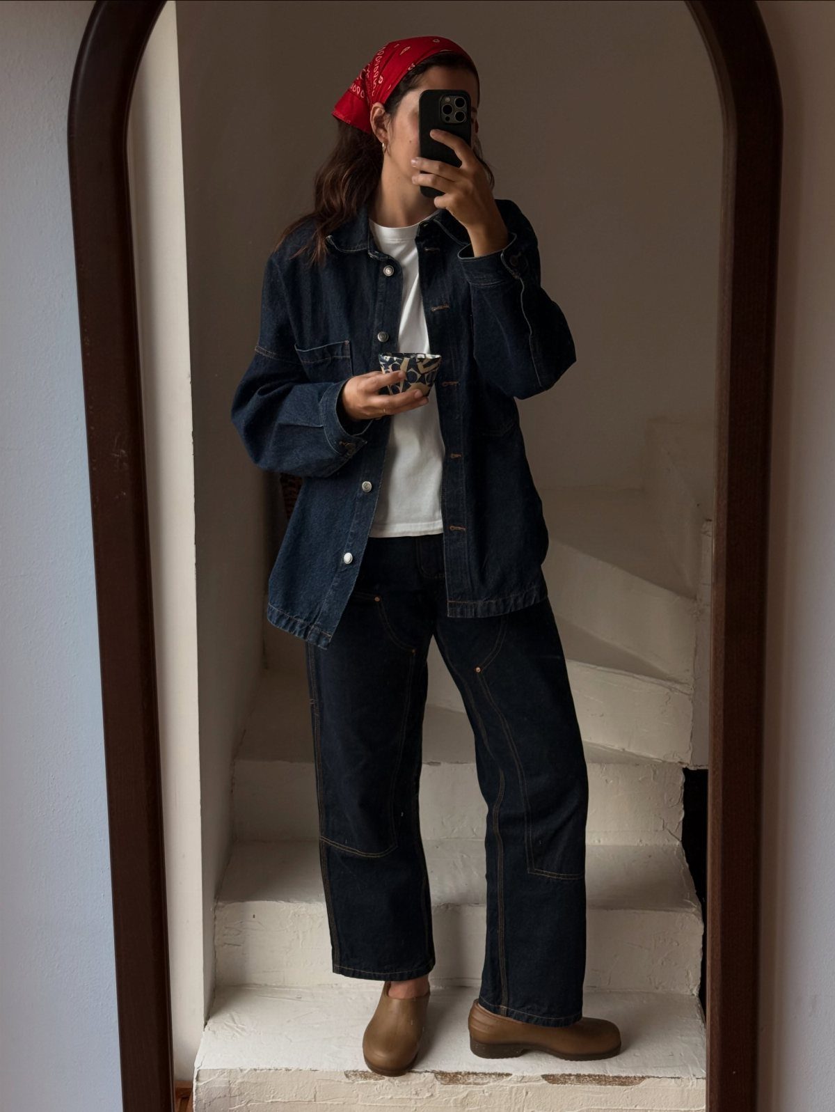 A person in a denim jacket, white t-shirt, and wide-leg jeans posing for a mirror selfie.
