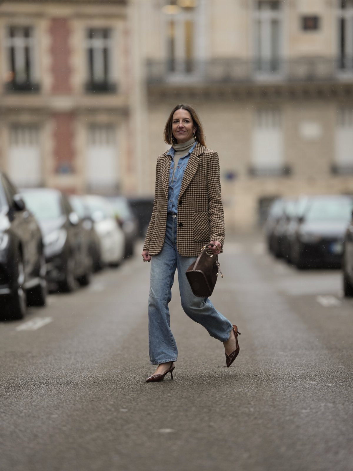 Woman walking on a city street wearing a patterned blazer, turtleneck, and wide-leg jeans.