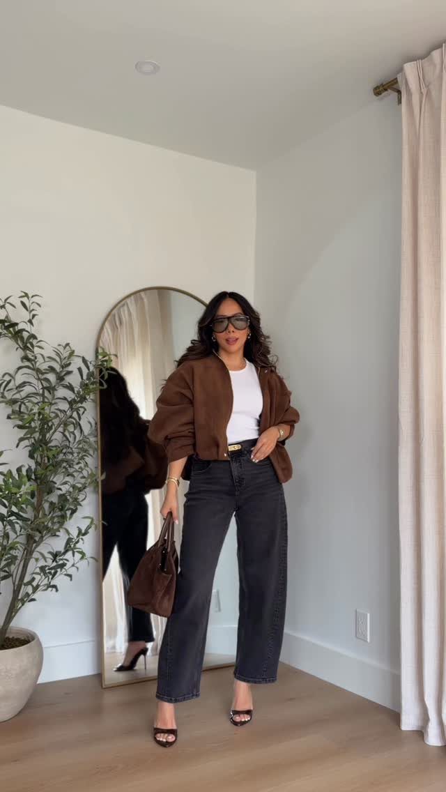 Woman in a brown jacket and dark wide-leg jeans posing in front of a mirror.