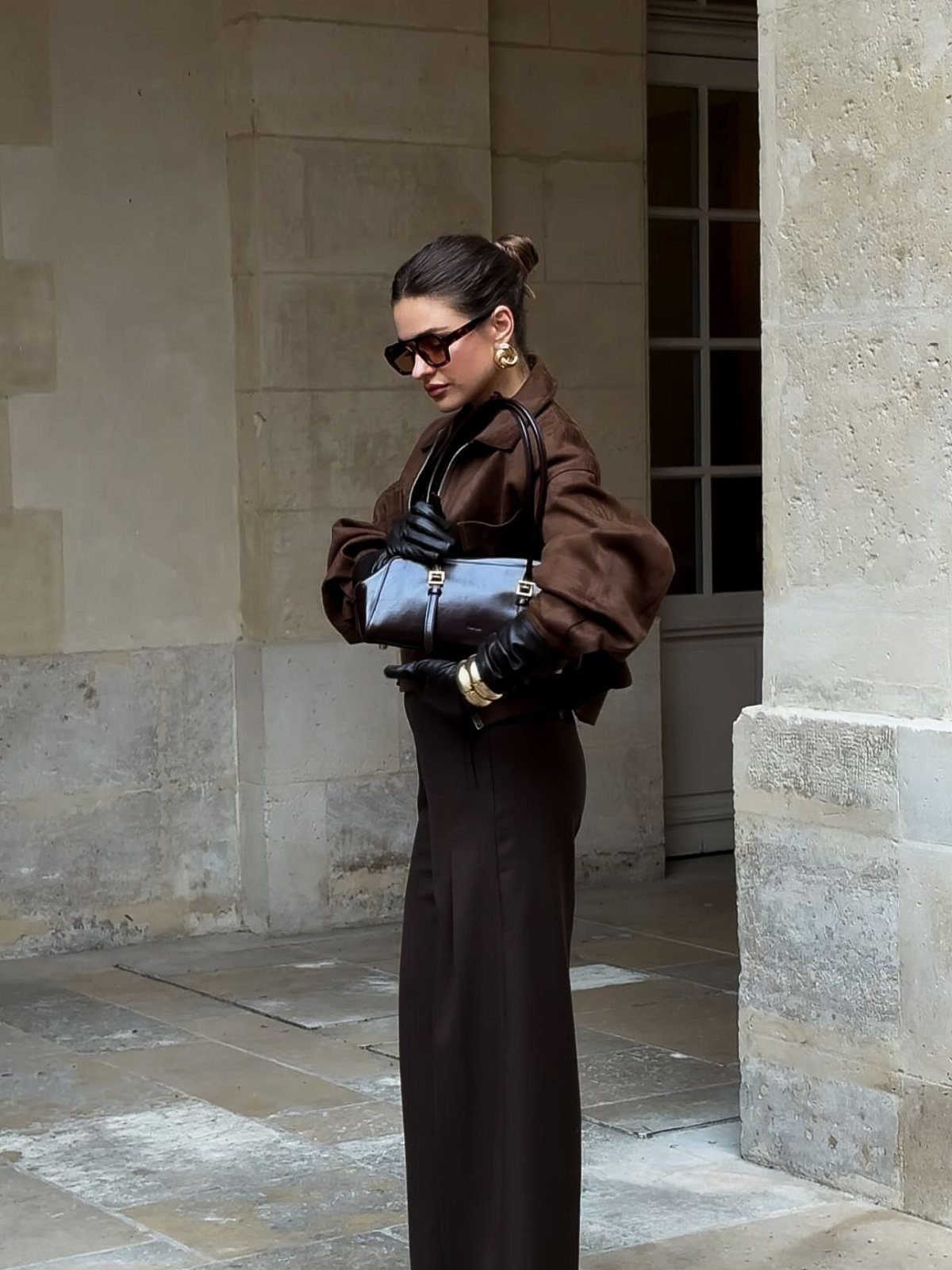 Woman wearing a monochrome dark brown outfit with a long skirt, voluminous top, and black leather gloves.