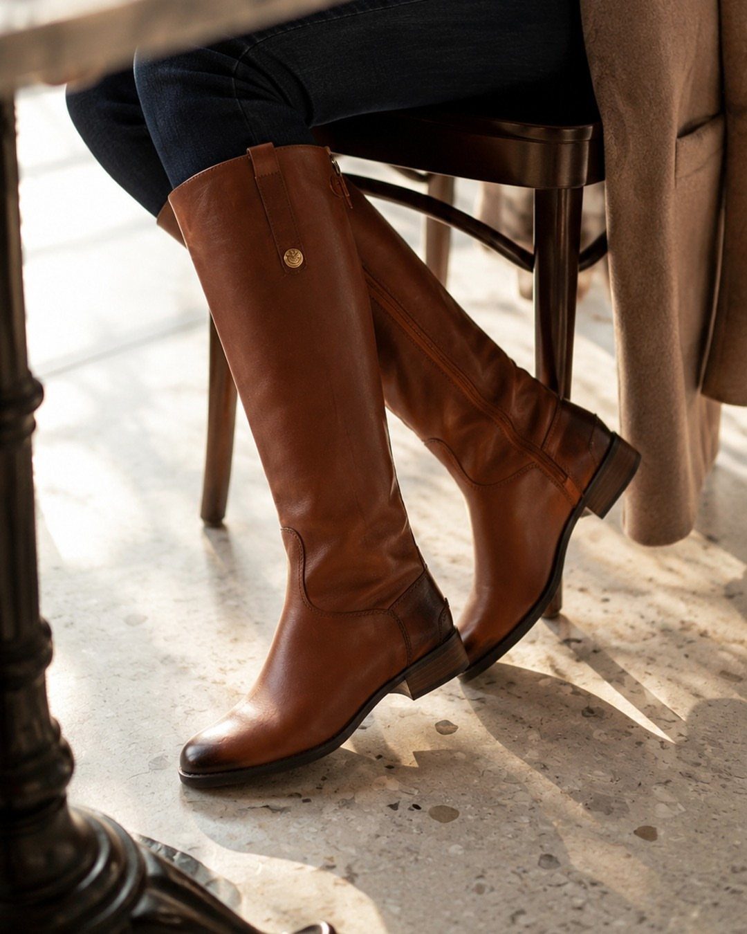 Tall cognac leather riding boots worn with dark blue denim jeans.