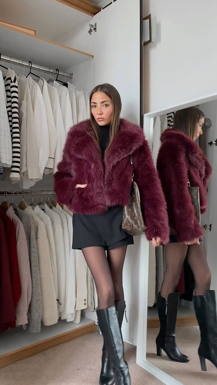 Woman wearing a maroon faux fur jacket, black turtleneck, shorts, and knee-high boots in a closet.