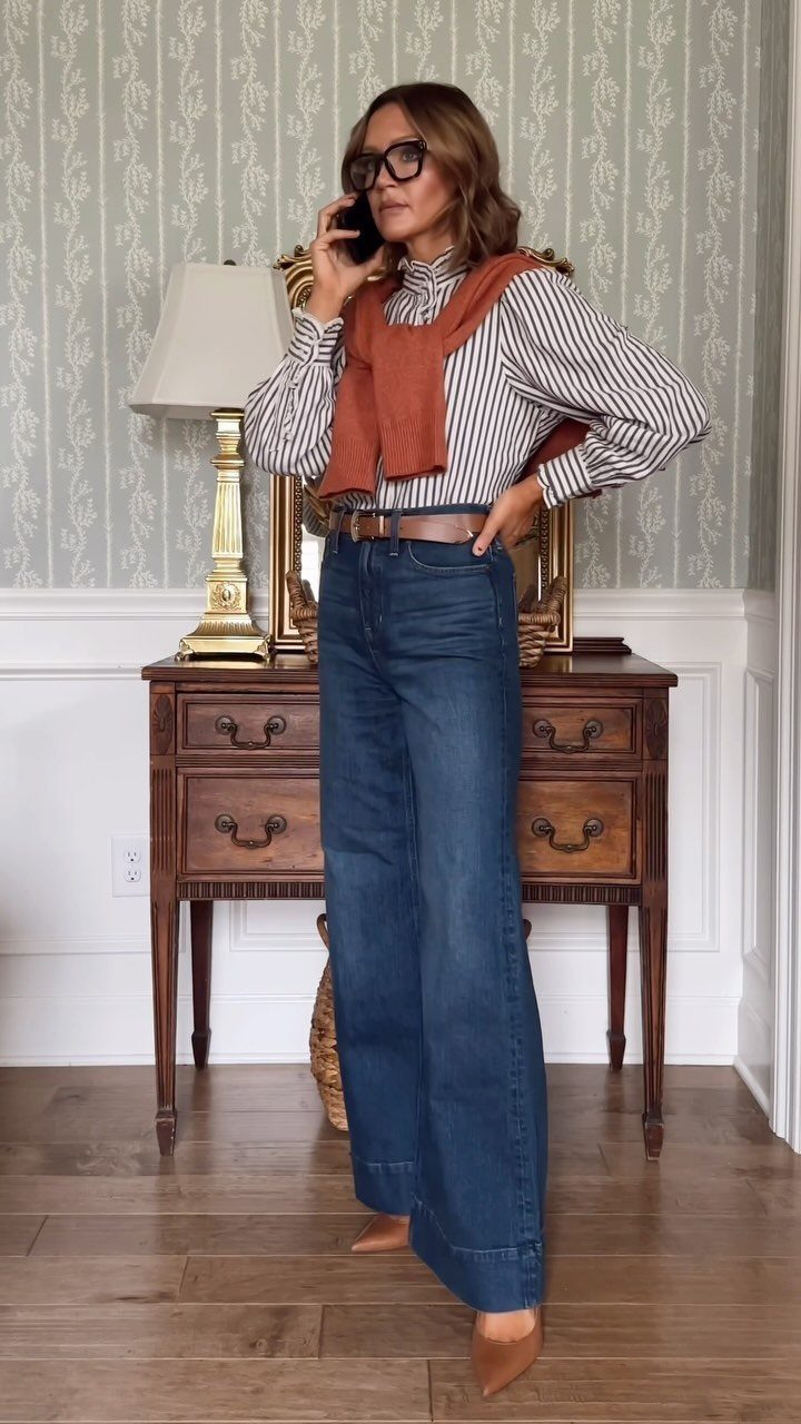 Woman wearing a striped shirt, orange sweater over shoulders, and wide-leg blue jeans.