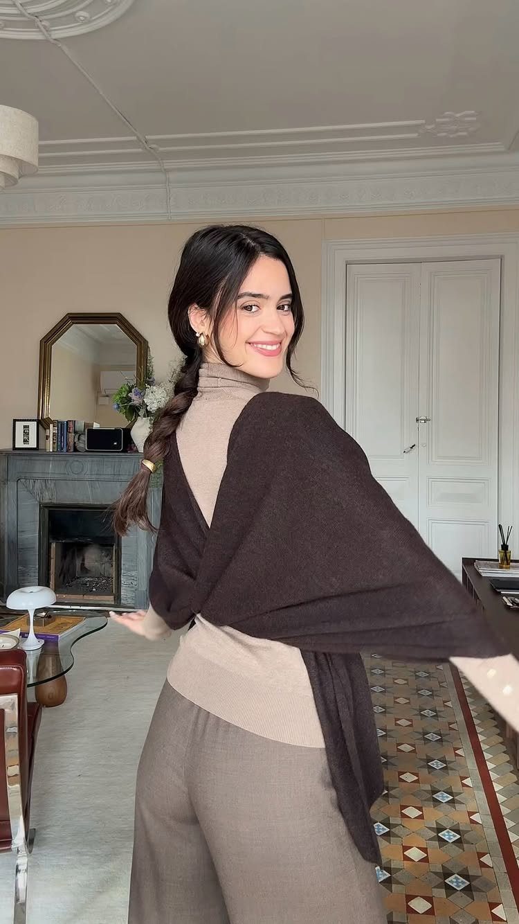 A woman wearing a tan turtleneck sweater and a dark brown knit shawl draped over her shoulders.