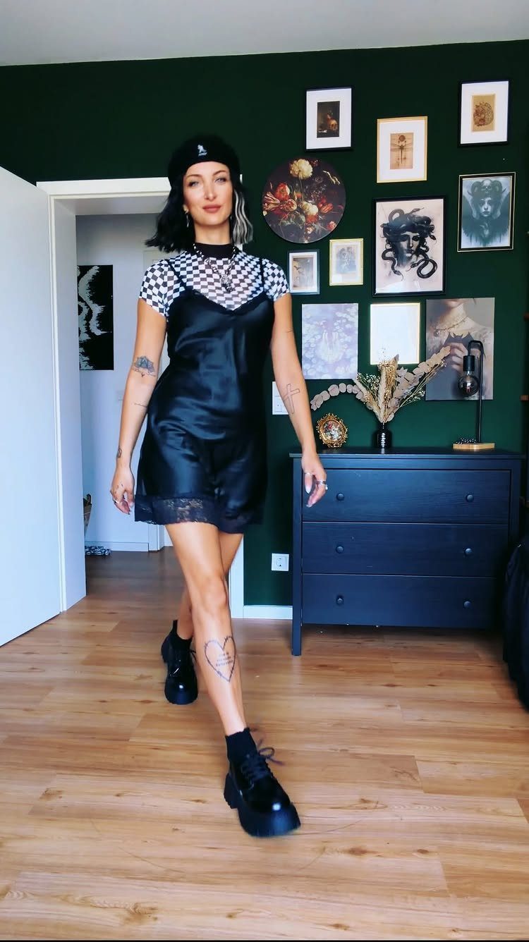 Woman wearing a black satin slipdress over a checkered top and black beret.