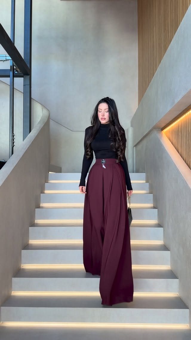 A woman wearing a black turtleneck and burgundy wide-leg trousers walking down stairs.