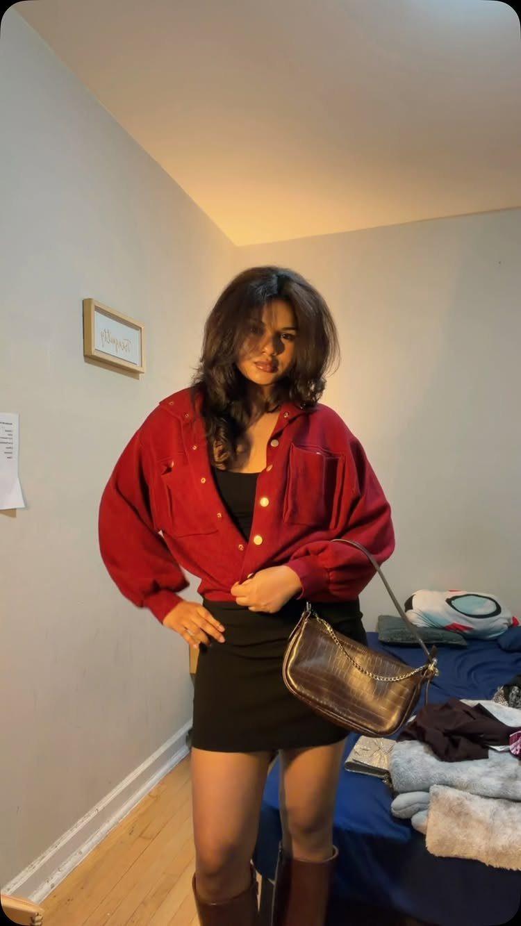A woman wearing a burgundy jacket and black dress posing in a room.