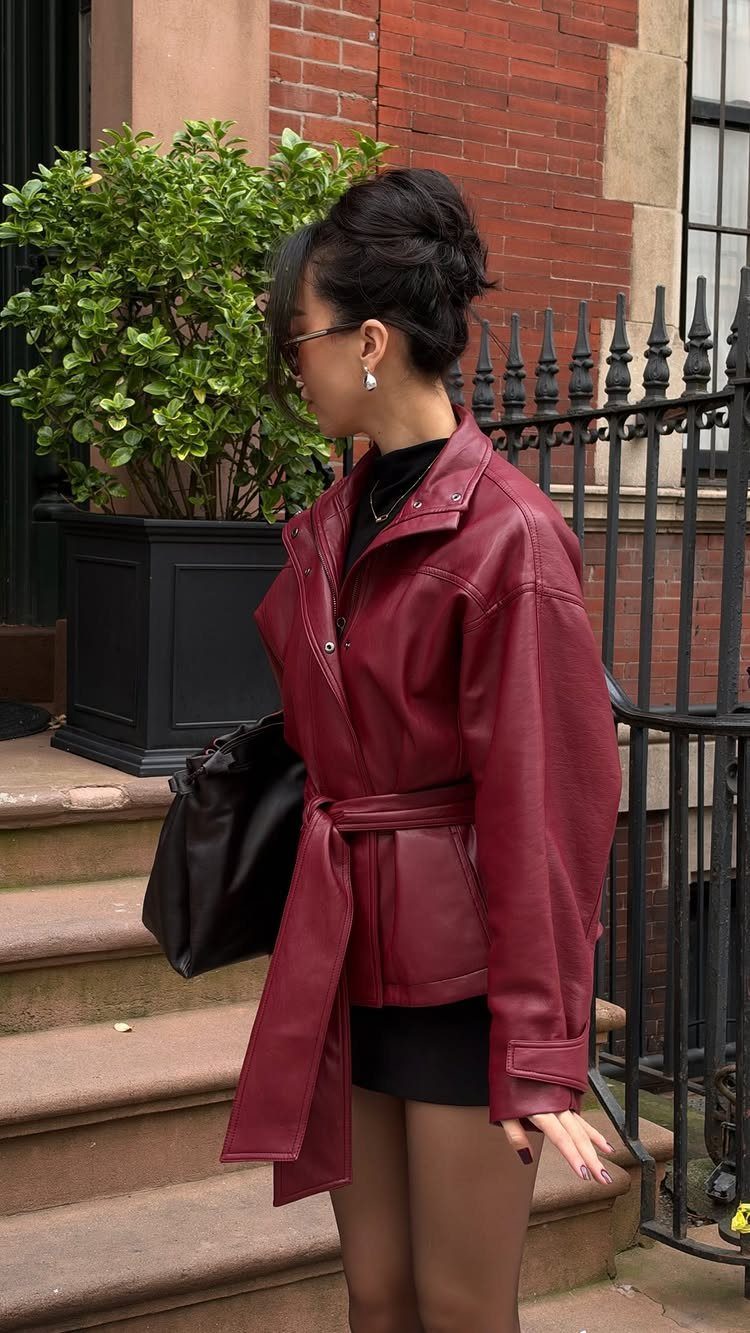 A woman in a burgundy leather jacket and black outfit standing on outdoor stone steps.