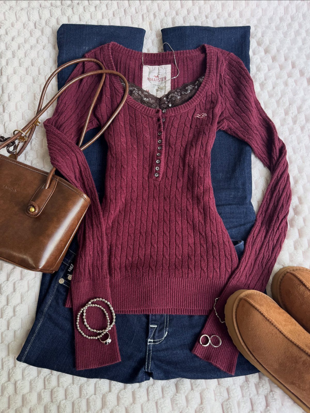 Burgundy ribbed long-sleeve top laid over dark blue denim jeans with accessories.