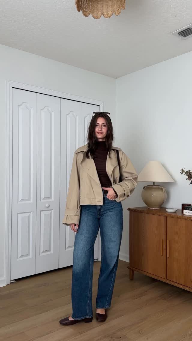 A woman wearing a burgundy turtleneck, beige jacket, and wide-leg blue jeans standing indoors.