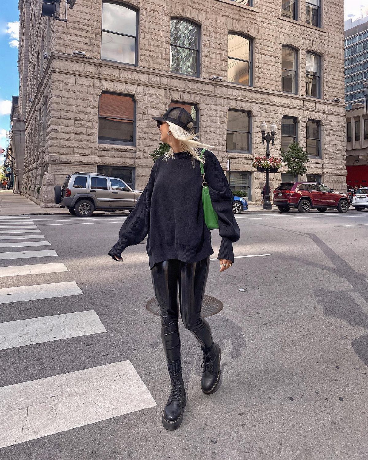 Woman in black oversized sweater and shiny black leggings walking across a city street.