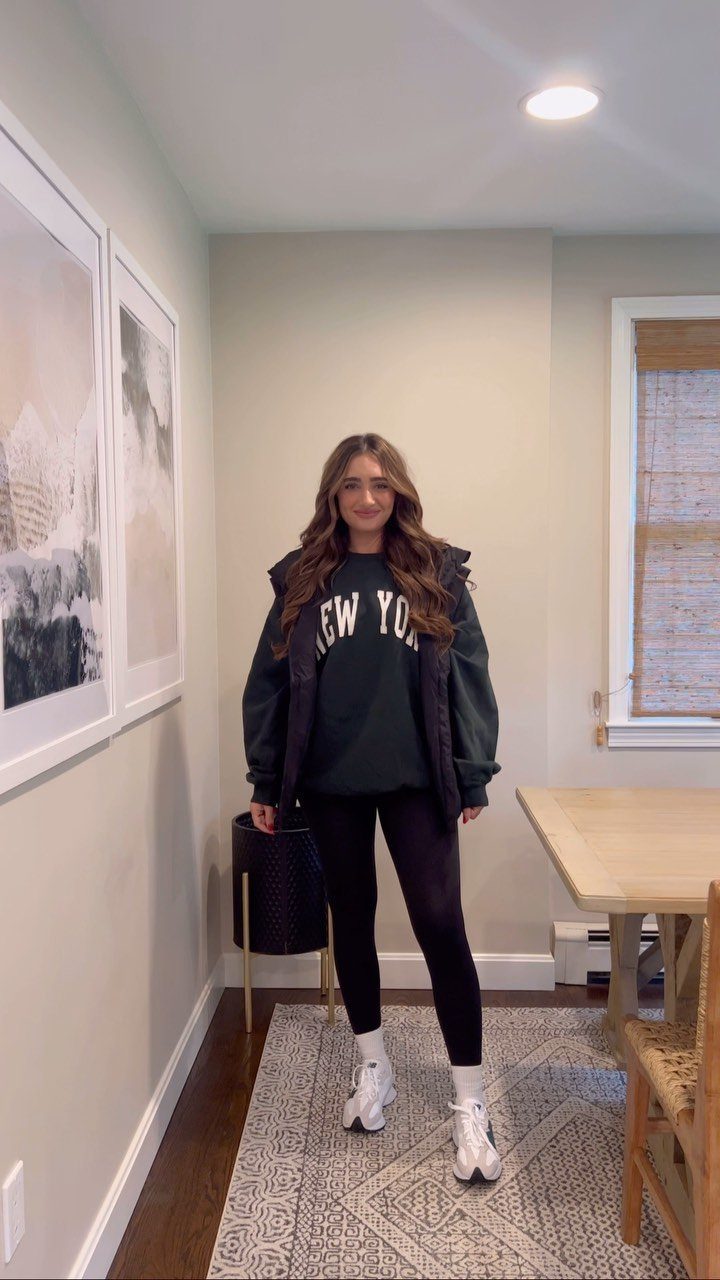A woman wearing a dark green graphic sweatshirt and black leggings with white sneakers.