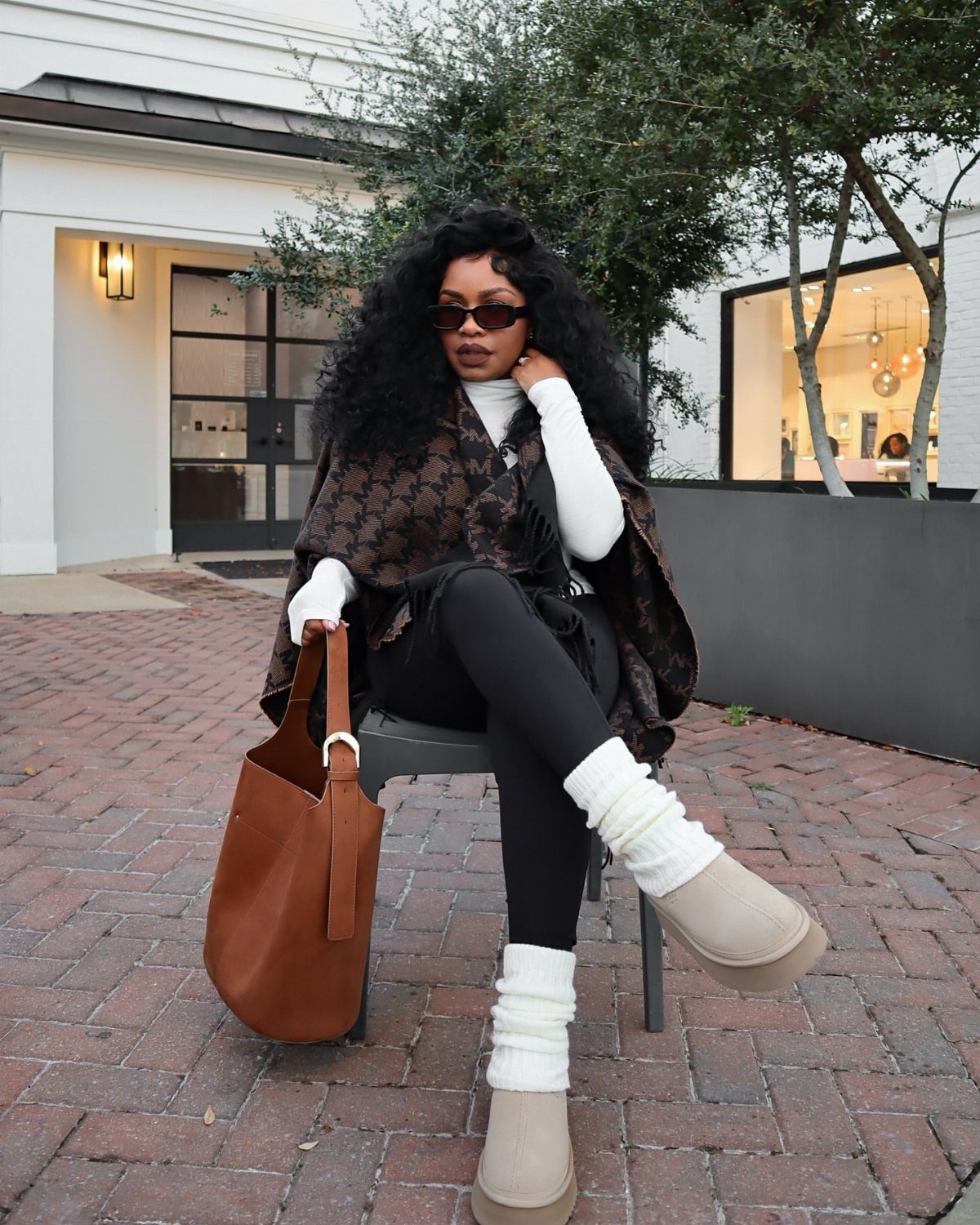 Woman sitting in a chair wearing black leggings, a patterned poncho, and white leg warmers.
