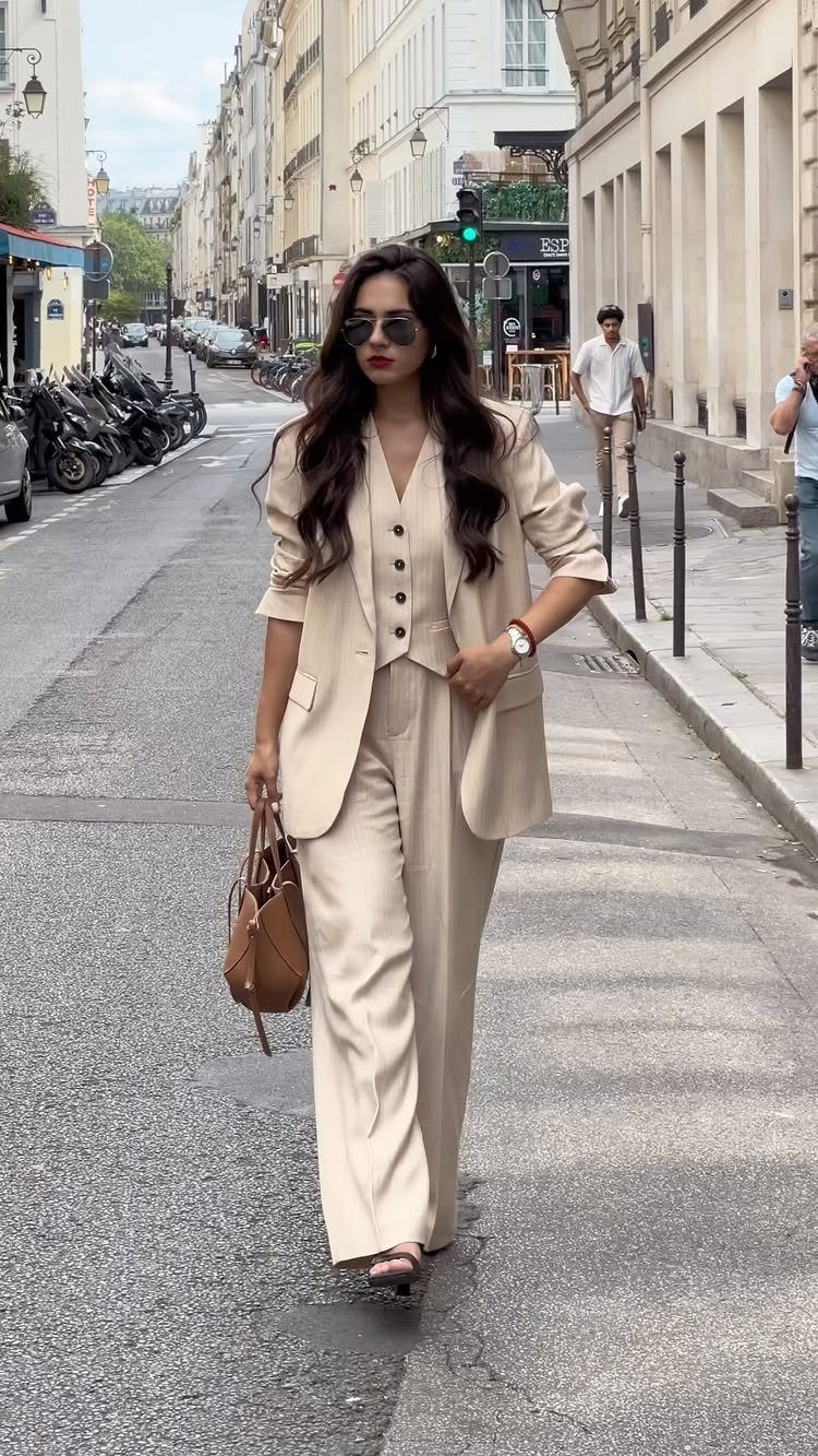 Woman walking on a city street wearing a beige blazer and matching trousers.