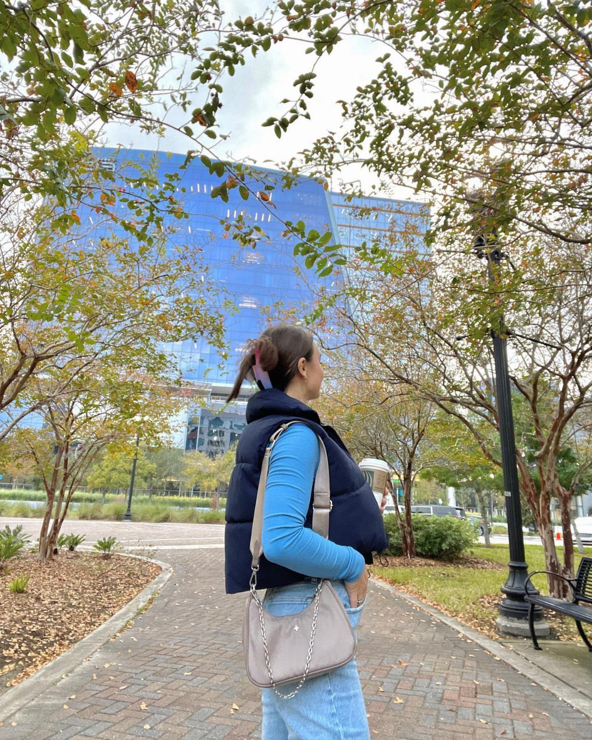 A woman wearing a navy blue puffer vest and light blue shirt walking outdoors.