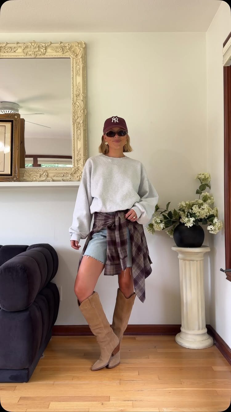 Woman wearing a grey sweatshirt and denim shorts with a plaid shirt tied around her waist.