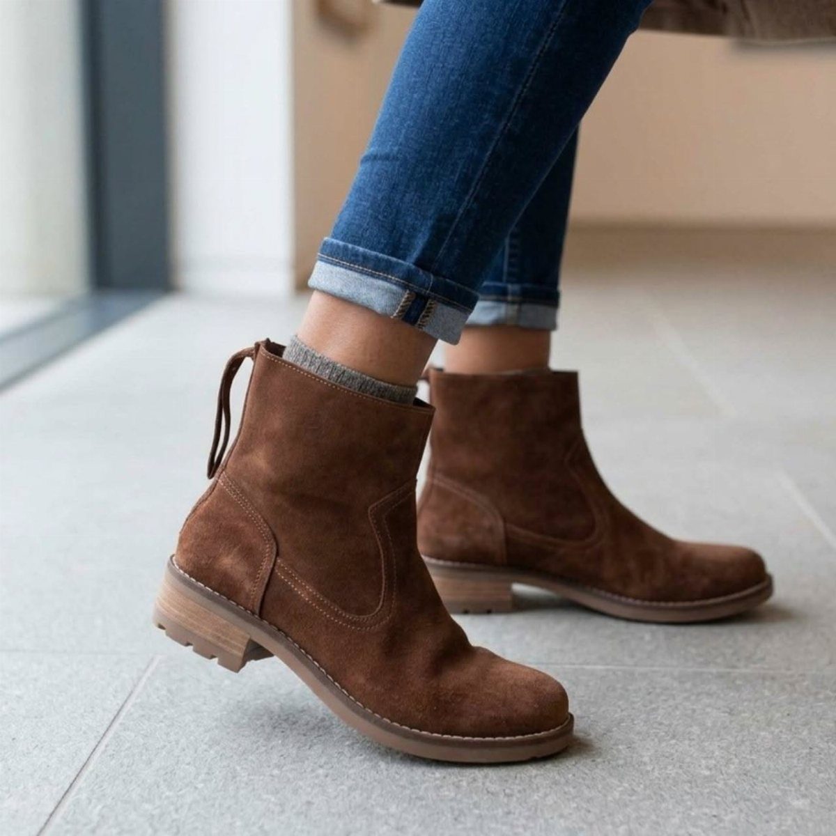 Brown suede ankle boots worn with blue denim jeans on a light floor.