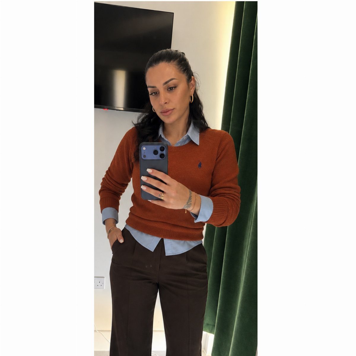 Woman in a burnt orange sweater and blue shirt posing for a mirror selfie.