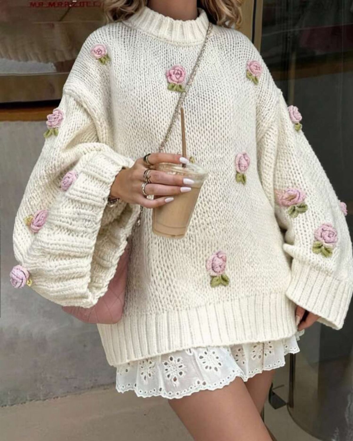 Person wearing a cream chunky knit sweater with pink rose embroidery and a white skirt.