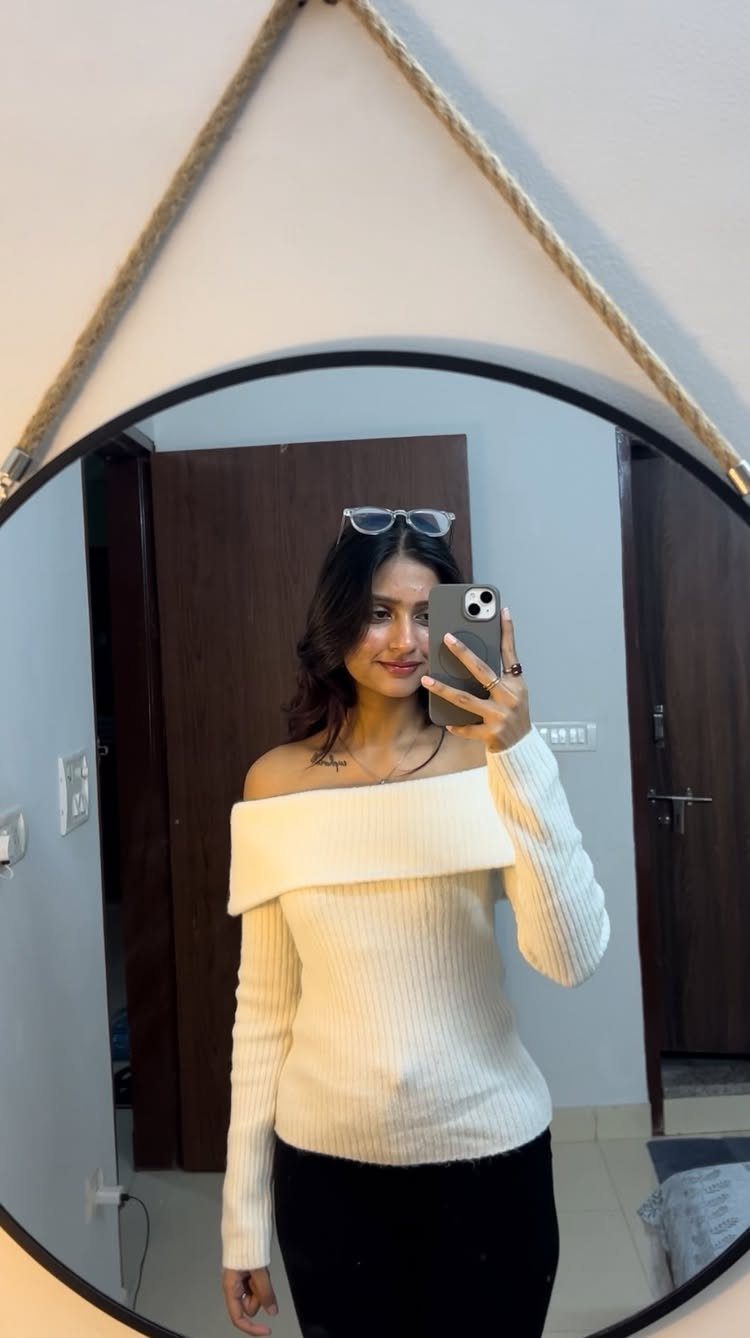 A woman posing in a mirror wearing a cream off-the-shoulder ribbed top.