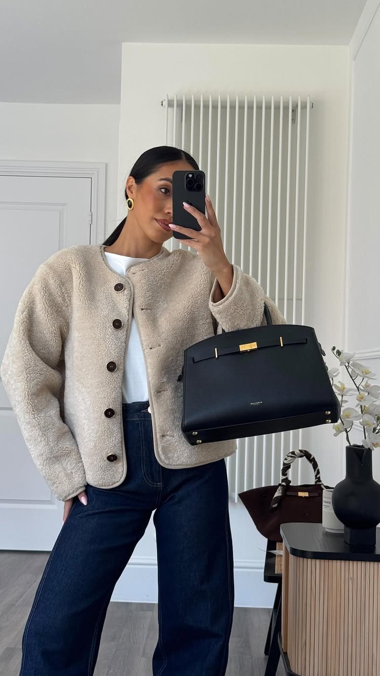 Woman in a cream textured jacket and dark blue wide-leg jeans taking a mirror selfie.