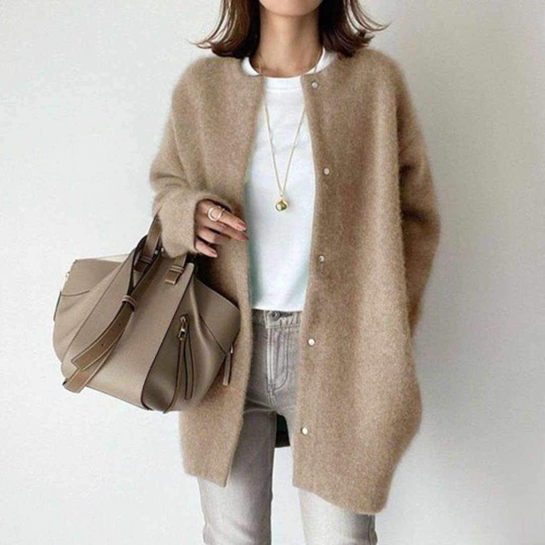 A woman wearing a long tan fuzzy cardigan, white t-shirt, and light grey jeans.