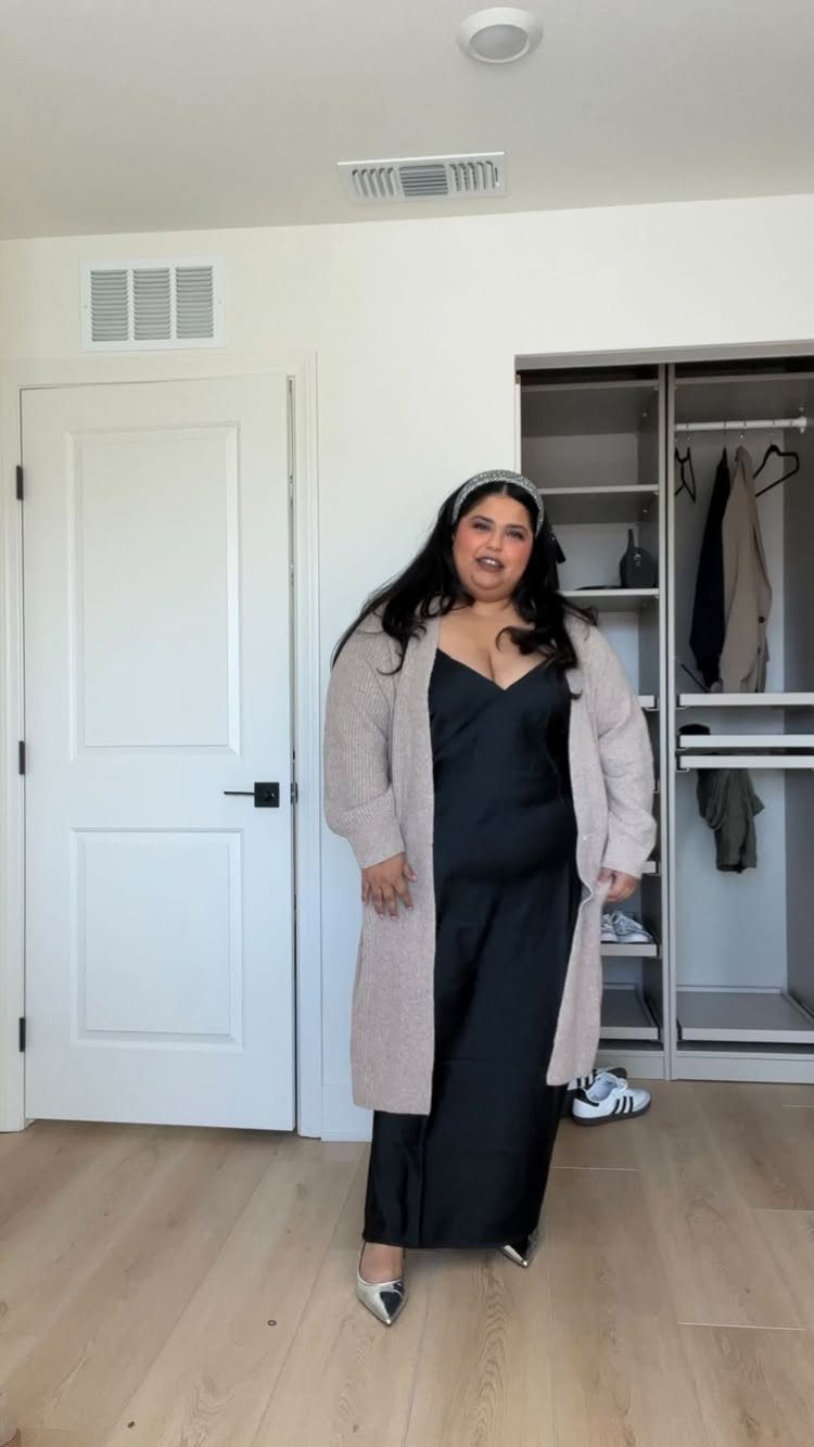 Woman wearing a long black satin slip dress and a light pink cardigan.