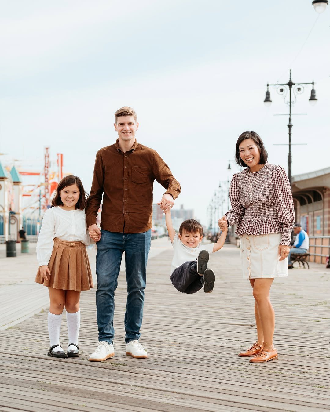 A smiling family of four posing together on a wooden boardwalk outdoors.