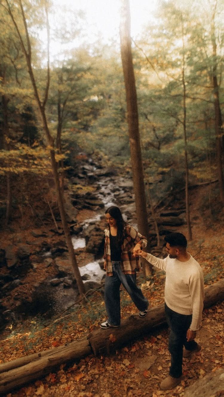 A man and woman walking through a forest near a small flowing stream.