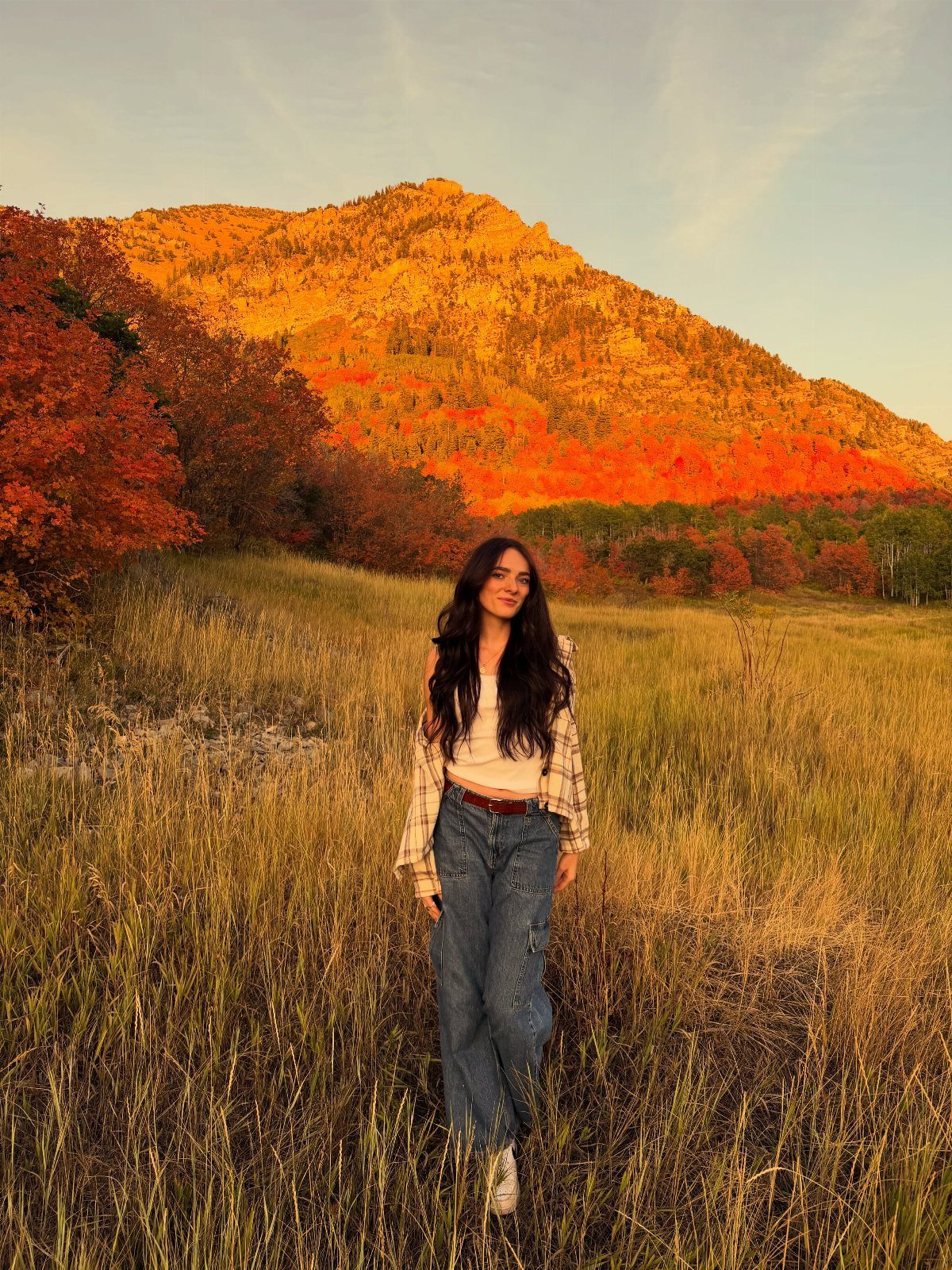 A woman standing in a golden field with a sunlit mountain in the background.