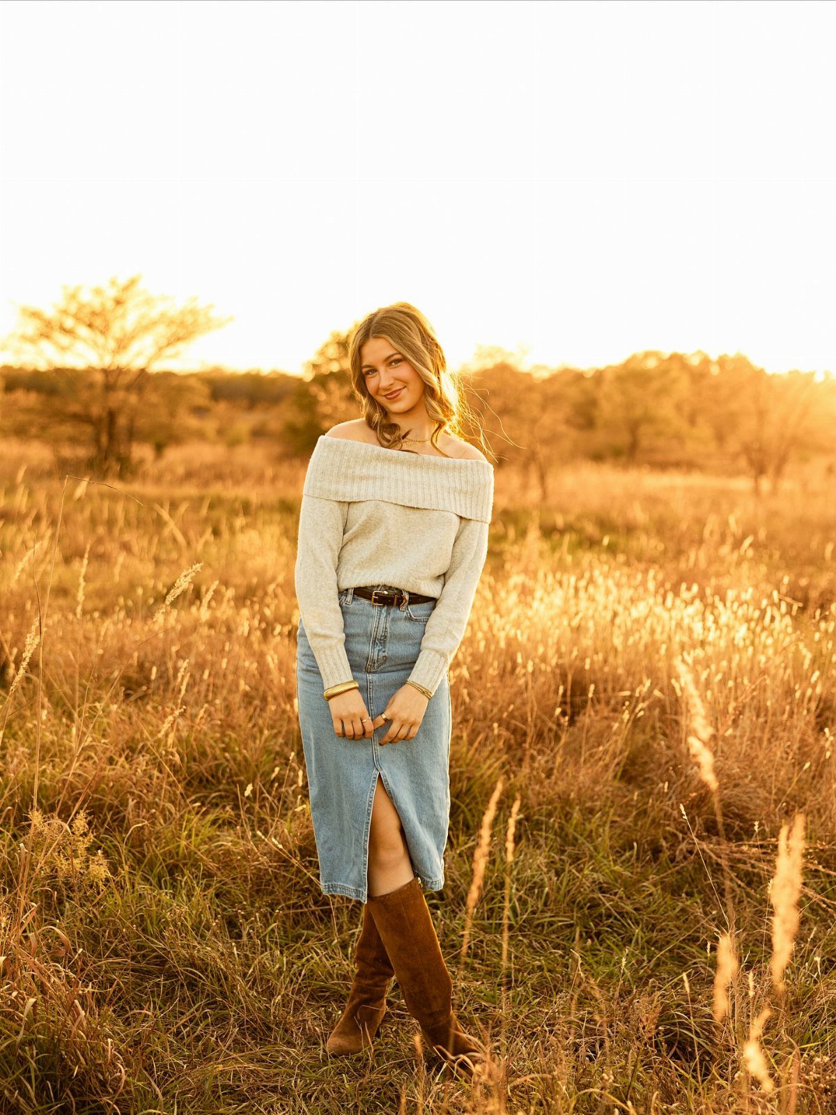 A woman in a cream sweater and denim skirt posing in a golden autumn field.