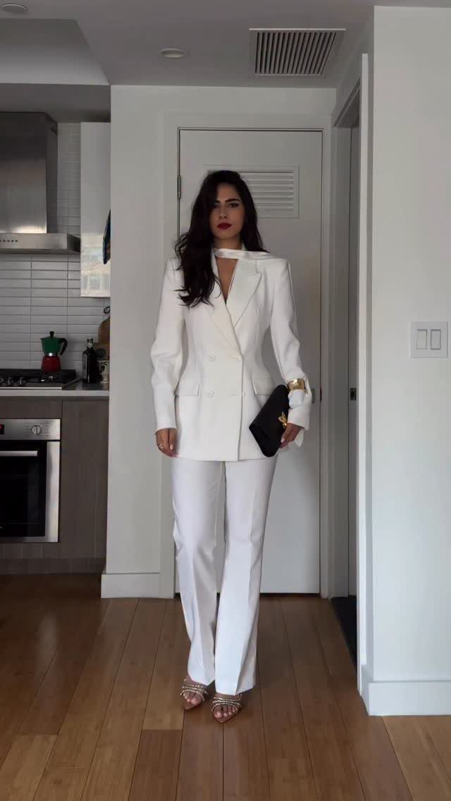 Woman wearing a white blazer and matching trousers posing in a modern room.
