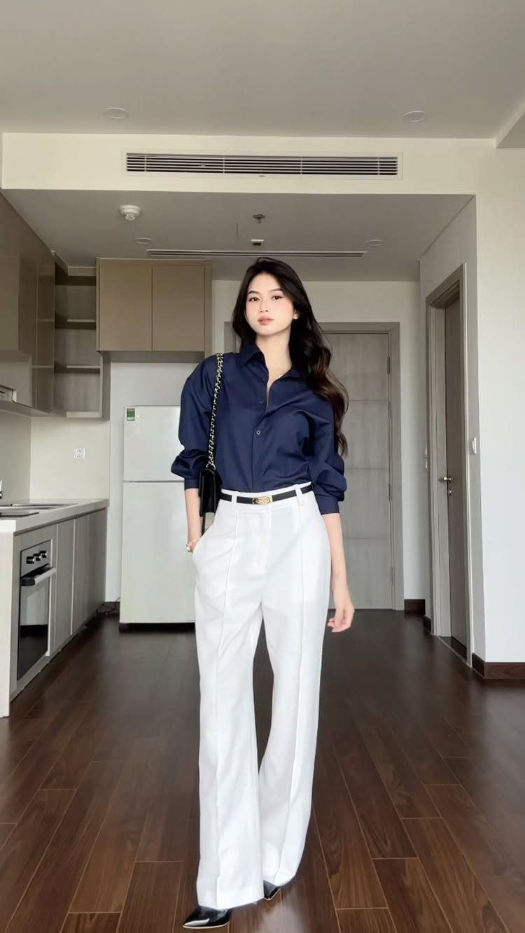 Woman posing in a navy long-sleeve blouse and white wide-leg trousers.