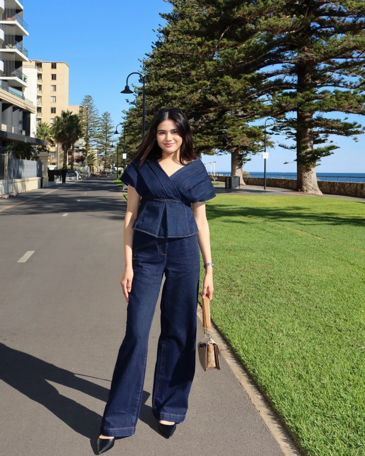 Woman posing outdoors in a dark denim peplum top and wide-leg denim trousers.
