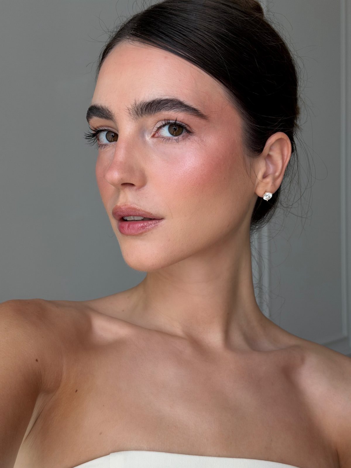 A woman with dark hair and natural makeup looking towards the camera against a grey background.
