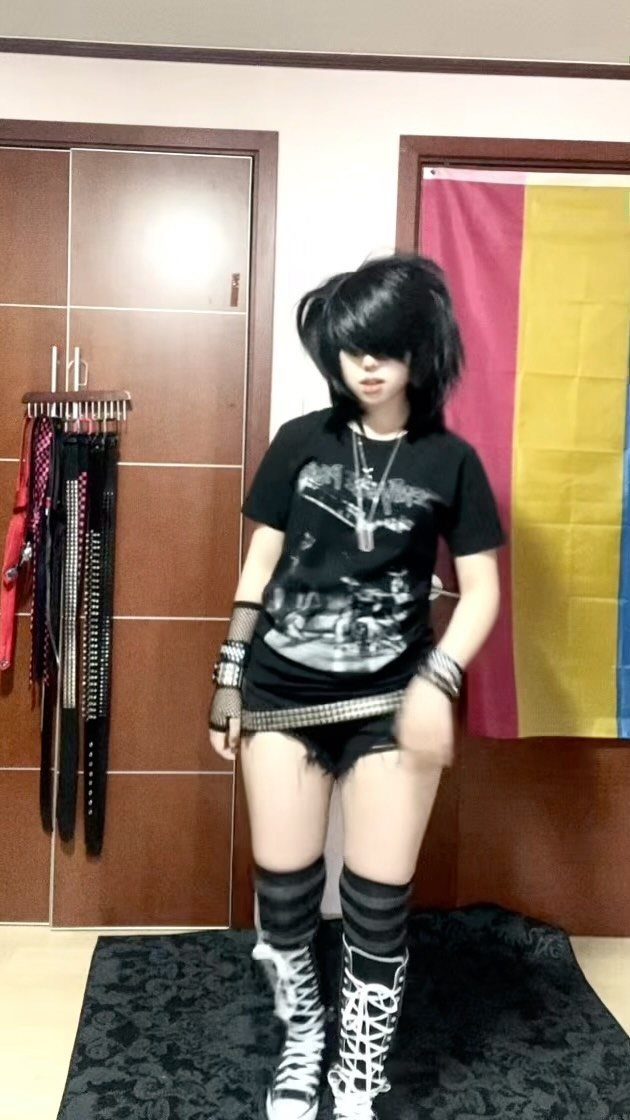 A person dressed in an emo-style outfit with black hair, graphic tee, and striped socks.