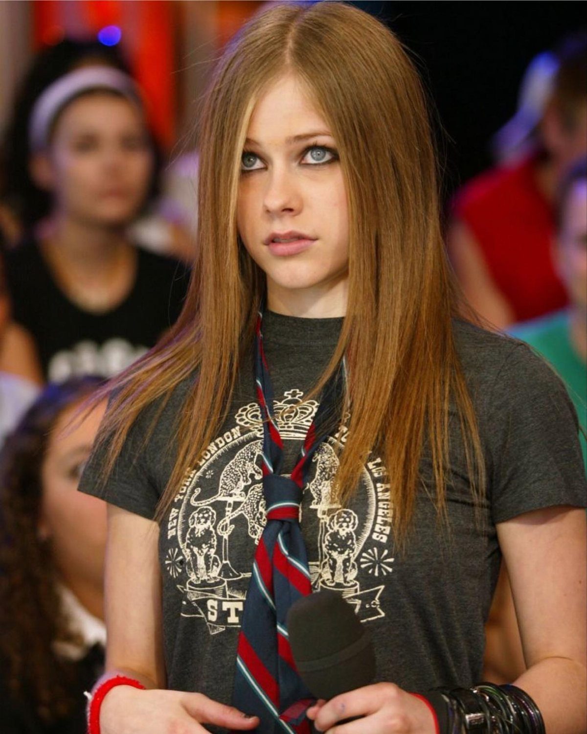 A young woman with long blonde hair wearing a grey graphic t-shirt and a striped necktie.