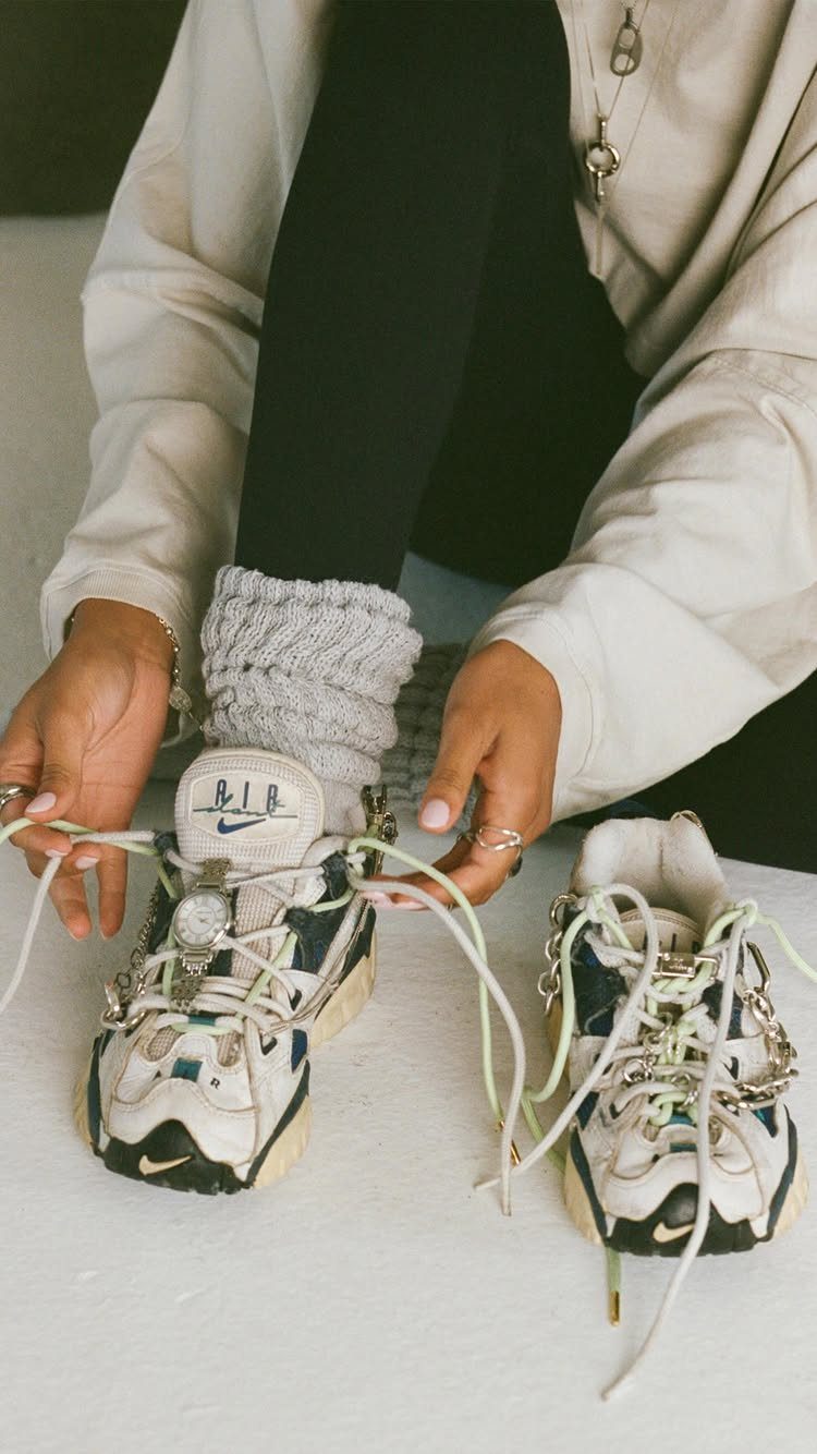 A person tying the laces of large, chunky white and black sneakers while wearing grey leg warmers.